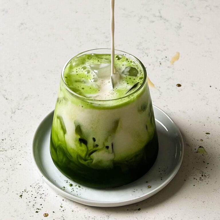 iced matcha latte in clear glass with oat milk and ice cubes